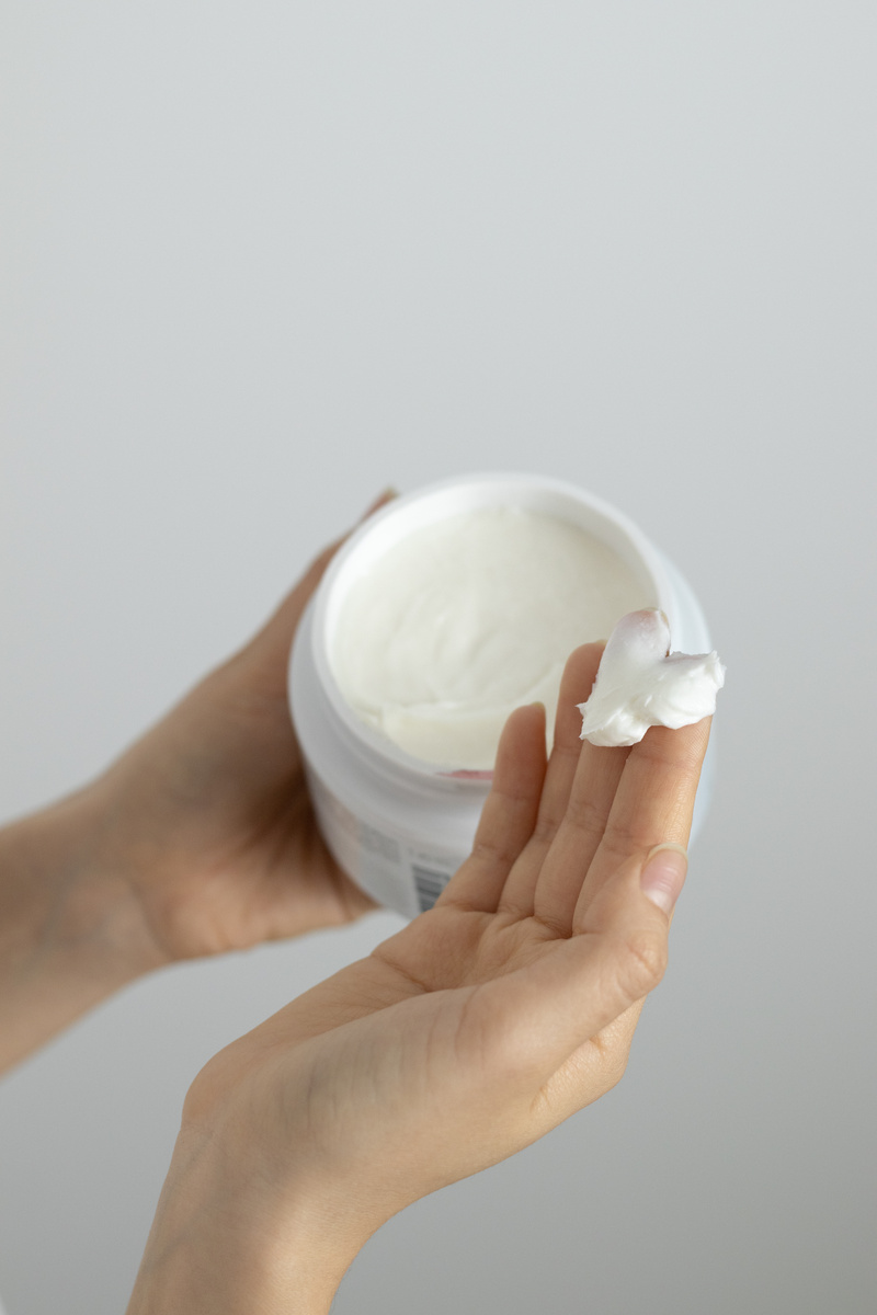 A Person Holding White Cream in White Plastic Container